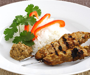 Photo of sate chicken kebabs with rice and red capsicum slices.
